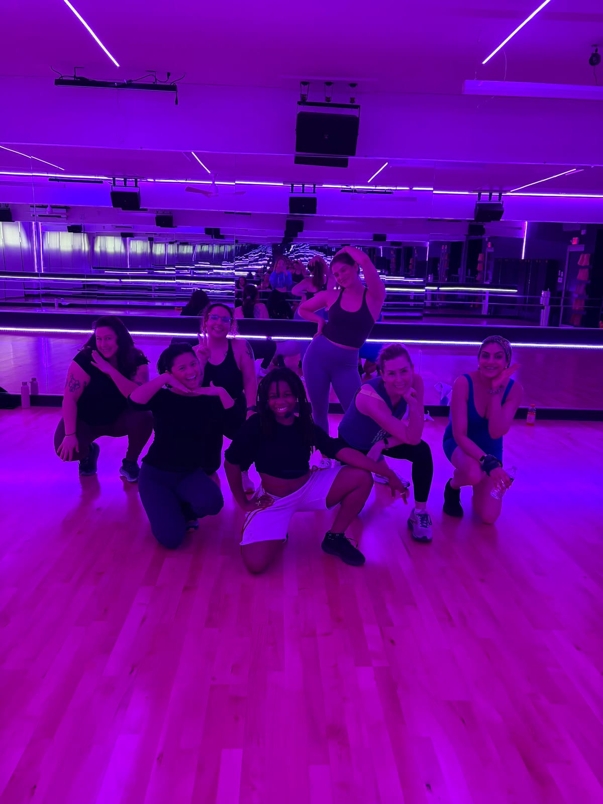 A group of 305 Fitness Philly dancers crowded together on the studio floor under purple light, laughing after class.