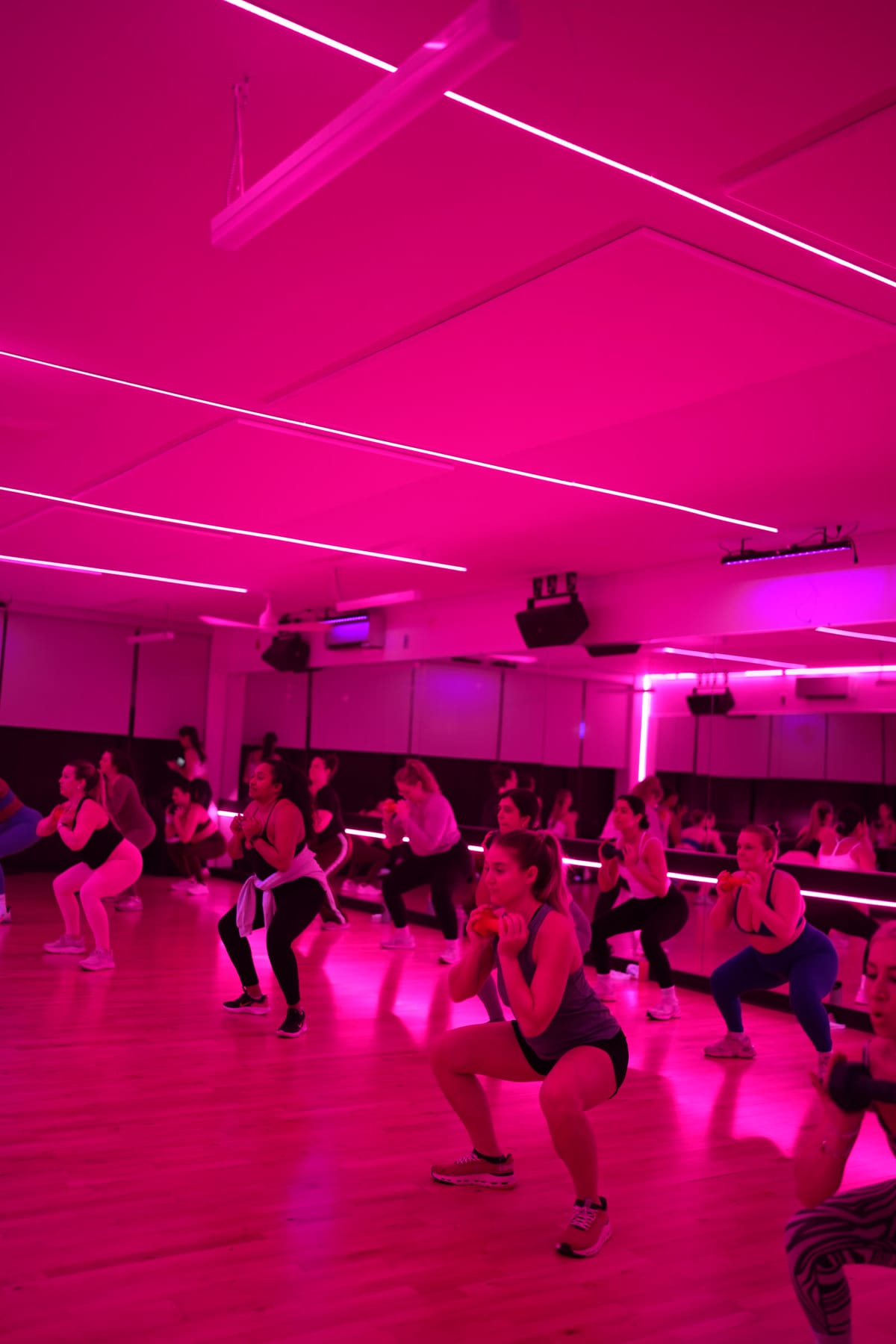A packed 305 Fitness Philly studio under deep pink light, the whole class dropped into the same low squat mid-routine.